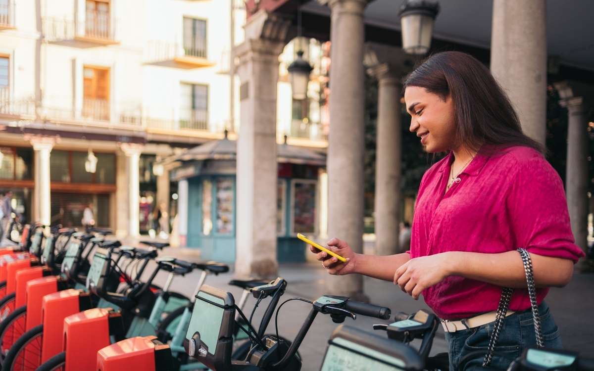 Woman using a smartphone to unlock a shared bicycle via a mobile payment app in a European city.