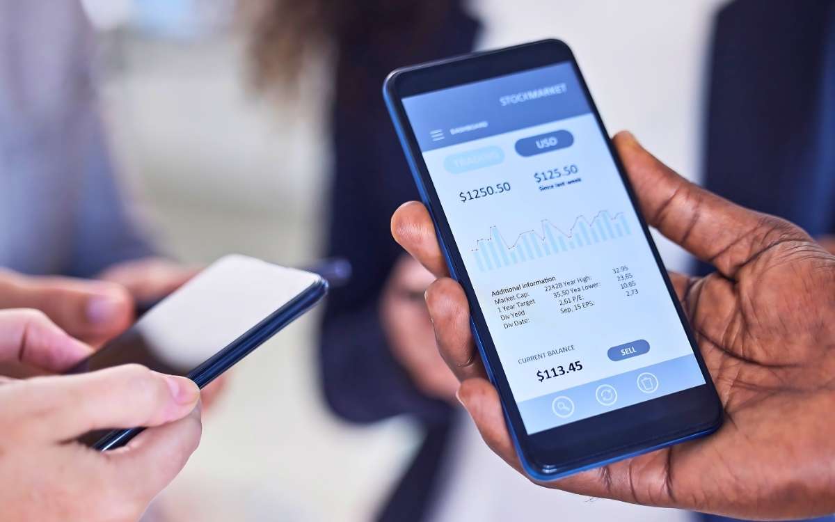Hands holding smartphones with digital banking and investment app showing stock market balance and transactions.