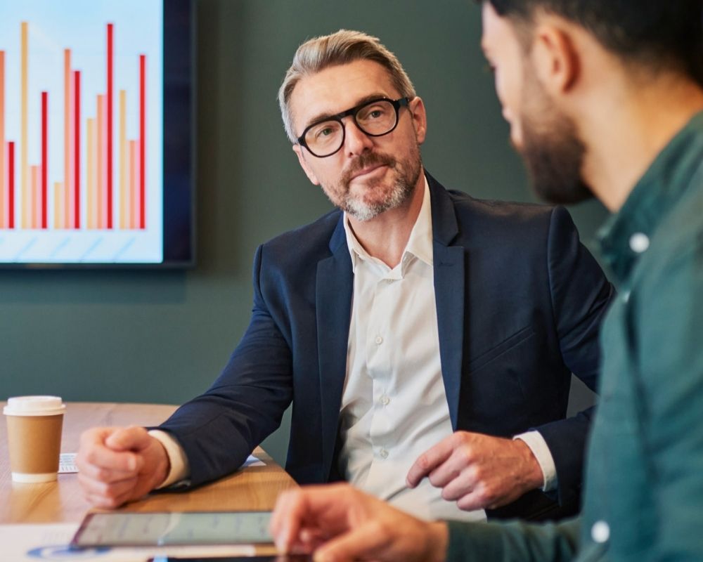 Paylume consultant discussing digital payments transformation with a client, with financial data charts displayed on screen.